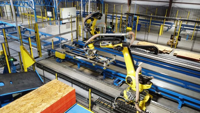 These two robots apply sheathing to FrameTec’s wall panels, fasten it and use routers to cut out the door and window openings. Credit: FrameTec